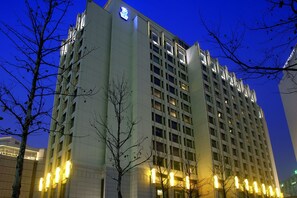 Un hotel de varios pisos con un letrero llamativo en la parte superior, ventanas amplias y luces iluminadas en la planta baja.