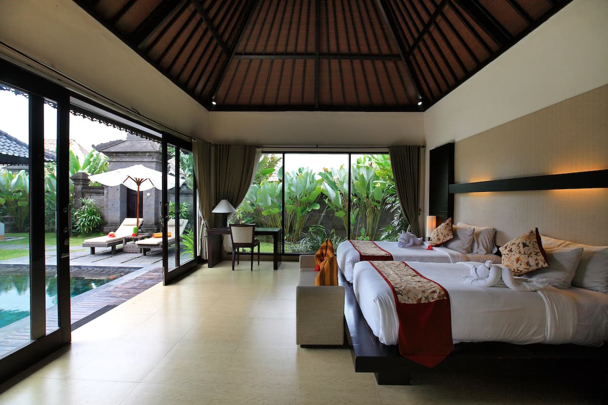 Ein Hotelzimmer mit zwei Betten, einer Sitzecke mit Tisch und Stühlen sowie Blick auf einen Pool und Garten.