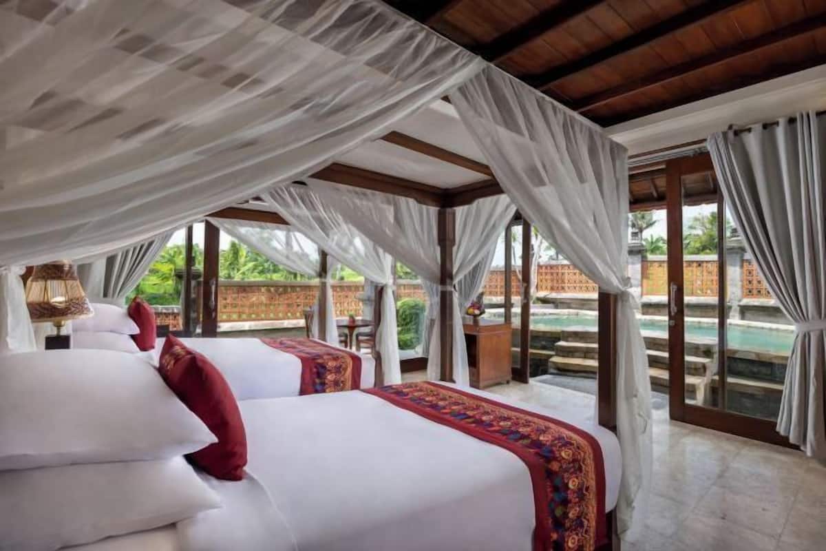 Ein Schlafzimmer mit Baldachinbett, Blick auf einen Pool und Holzboden.