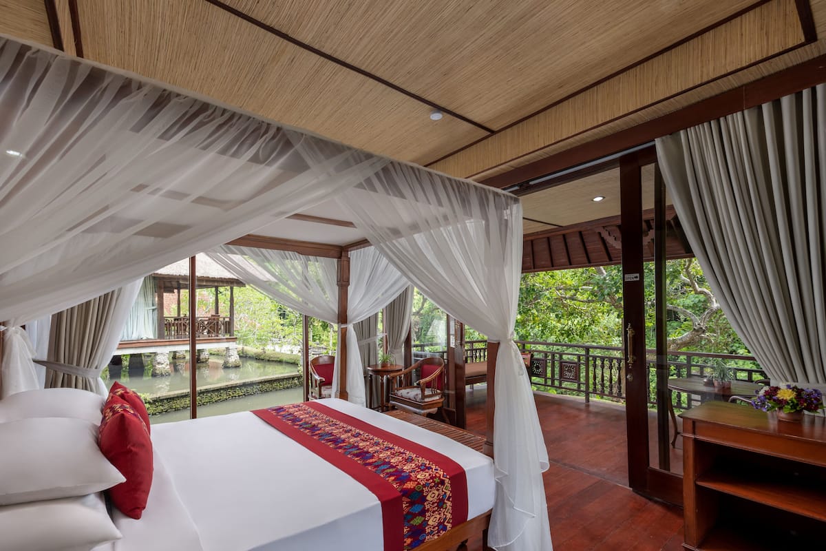 Ein Schlafzimmer mit Bett, Baldachin und Blick auf einen Pool sowie eine Sitzgelegenheit im Freien.