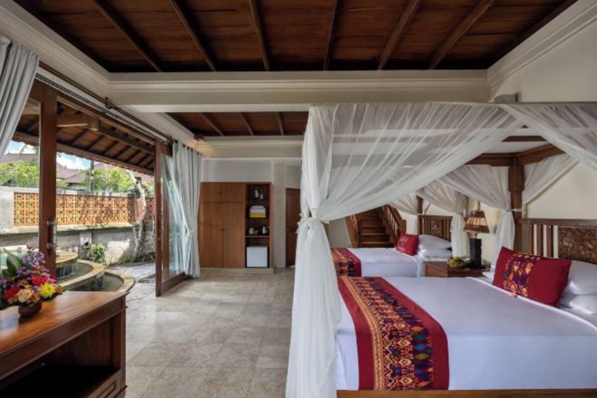 Una habitación con una cama bajo un dosel, un escritorio de madera con un florero y vistas a un jardín.