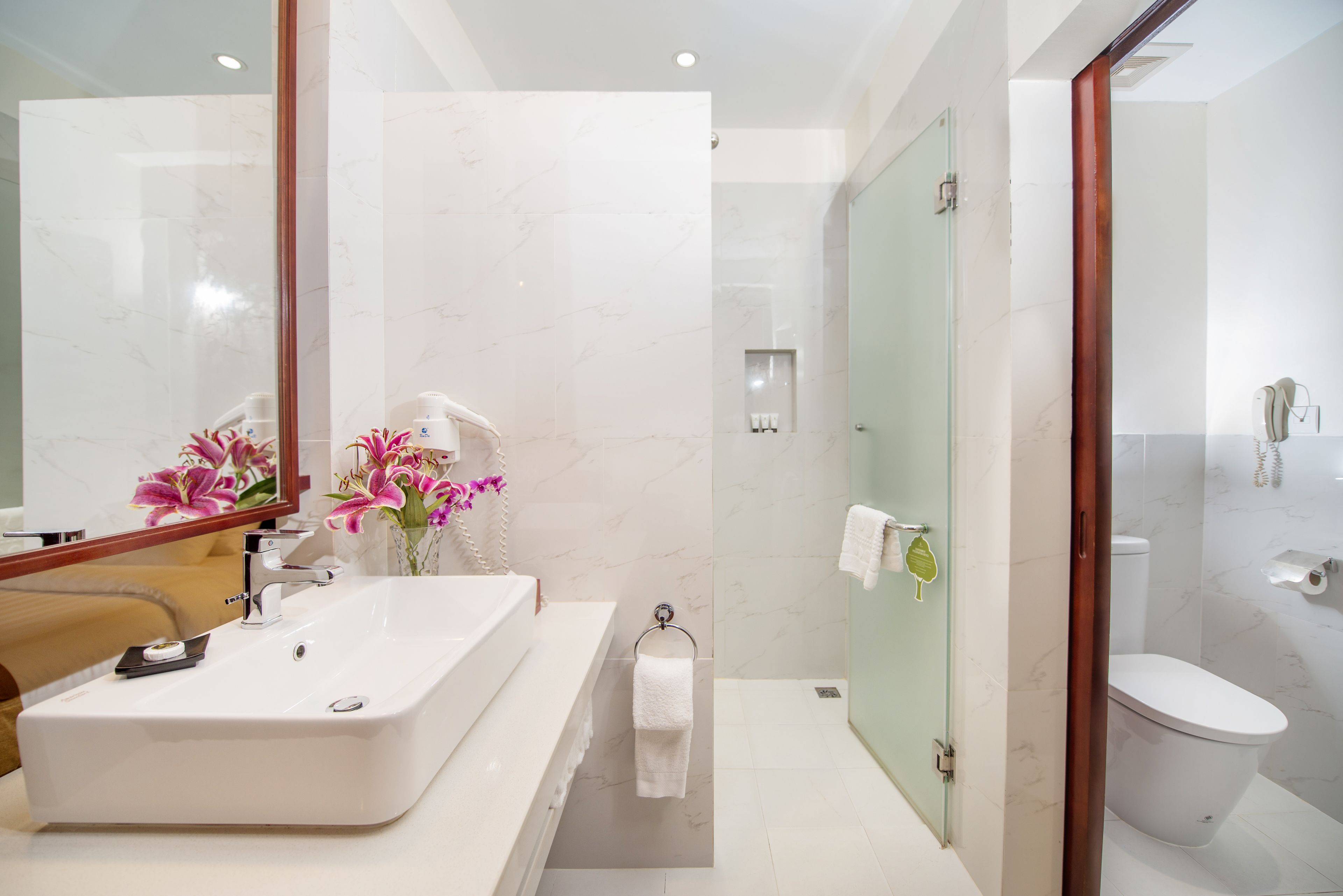 A modern bathroom with a large mirror, a white sink, a glass shower enclosure, and a toilet.