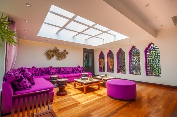 A modern living room with a large skylight, a purple sofa, wooden flooring, and decorative wall panels.