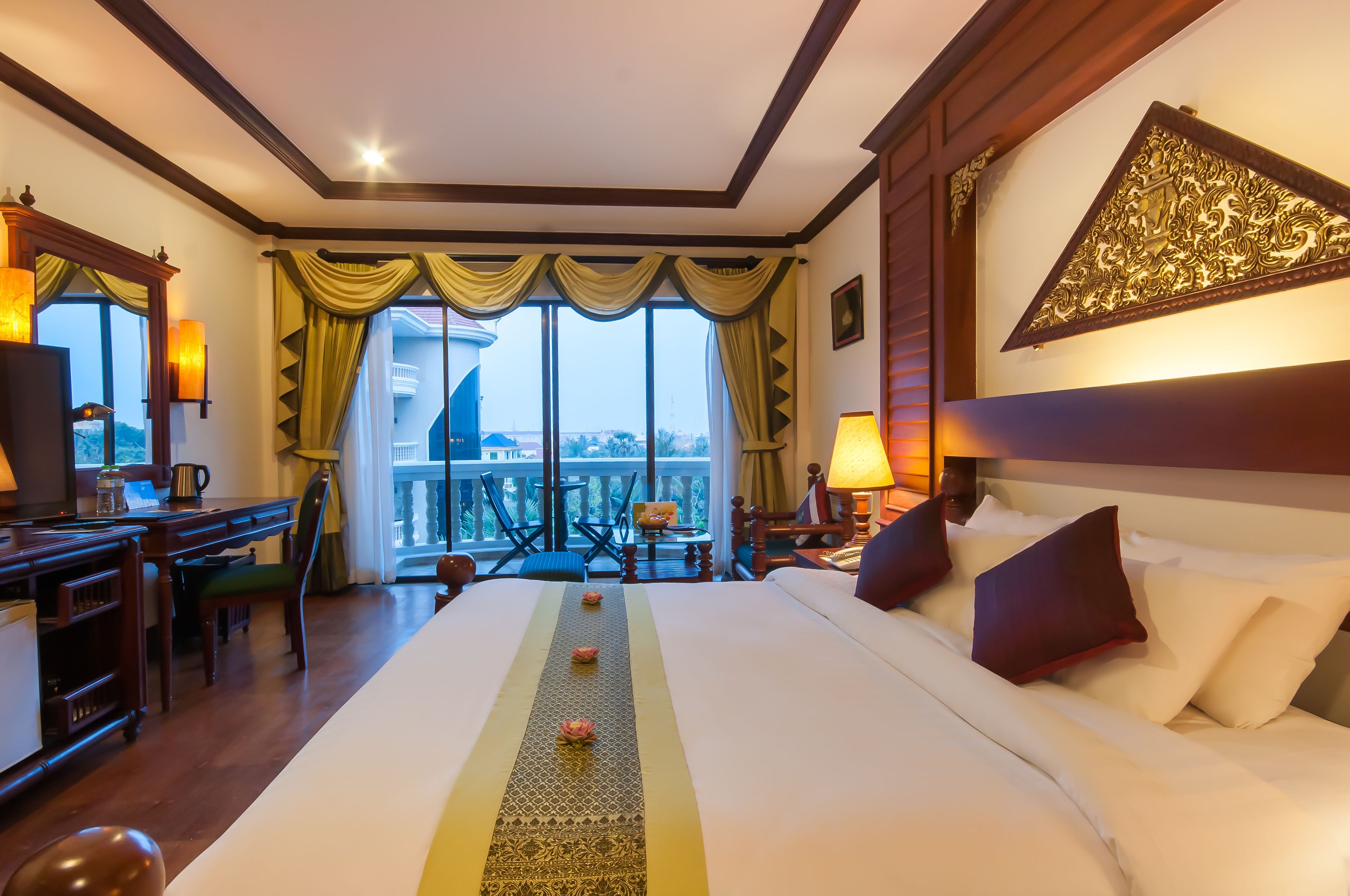 A hotel room with a large bed, a desk, and a balcony with a view.
