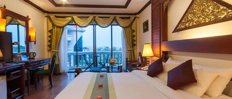 A hotel room with a large bed, a desk, and a balcony with a view.