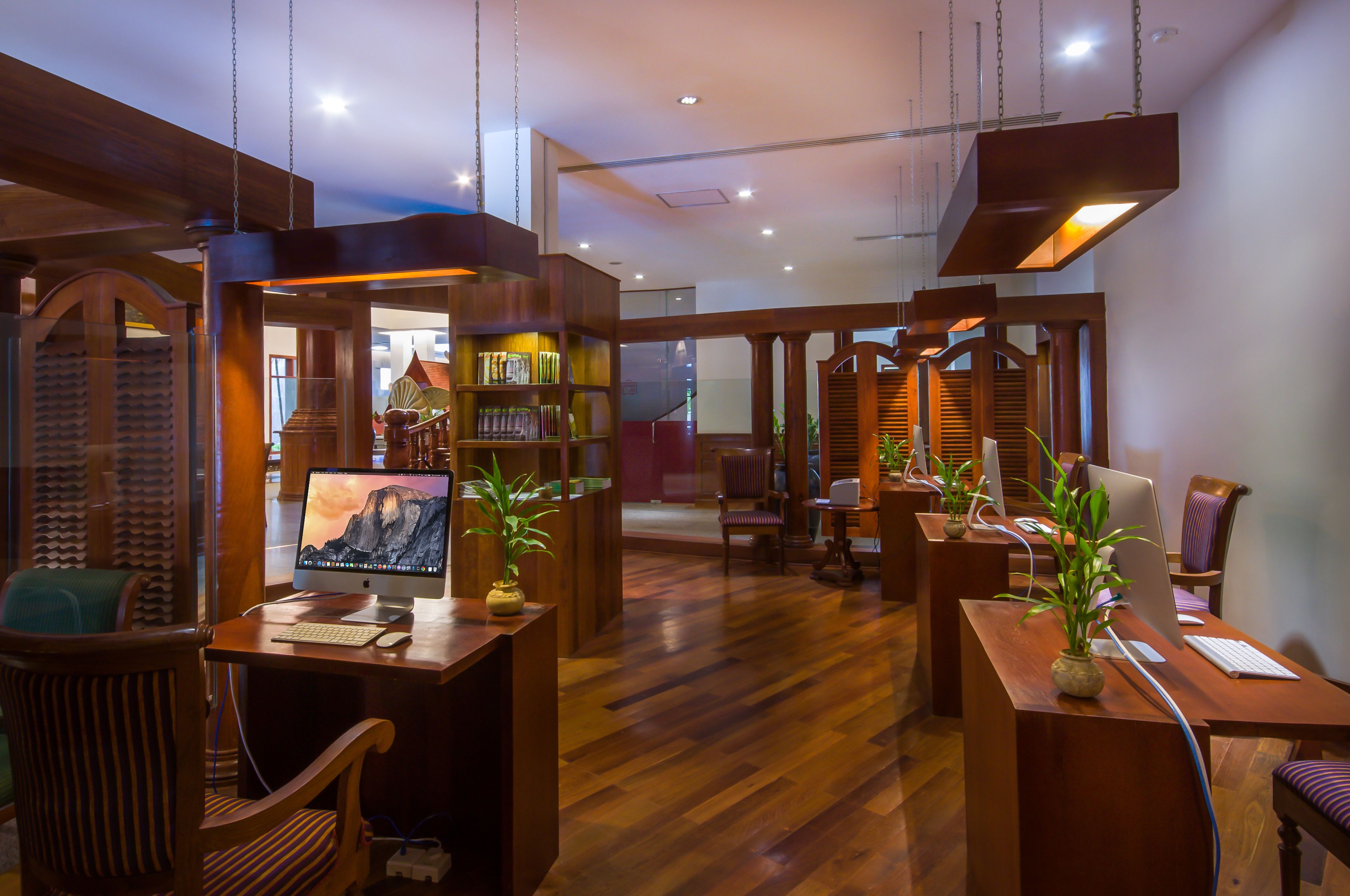 A modern hotel lobby with wooden furniture, a reception desk, and a staircase leading to the upper floor.