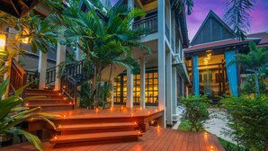 A wooden deck with steps leading to a covered area, surrounded by lush greenery and a building with a balcony. - Borei Angkor Resort & Spa (Siem Reap)