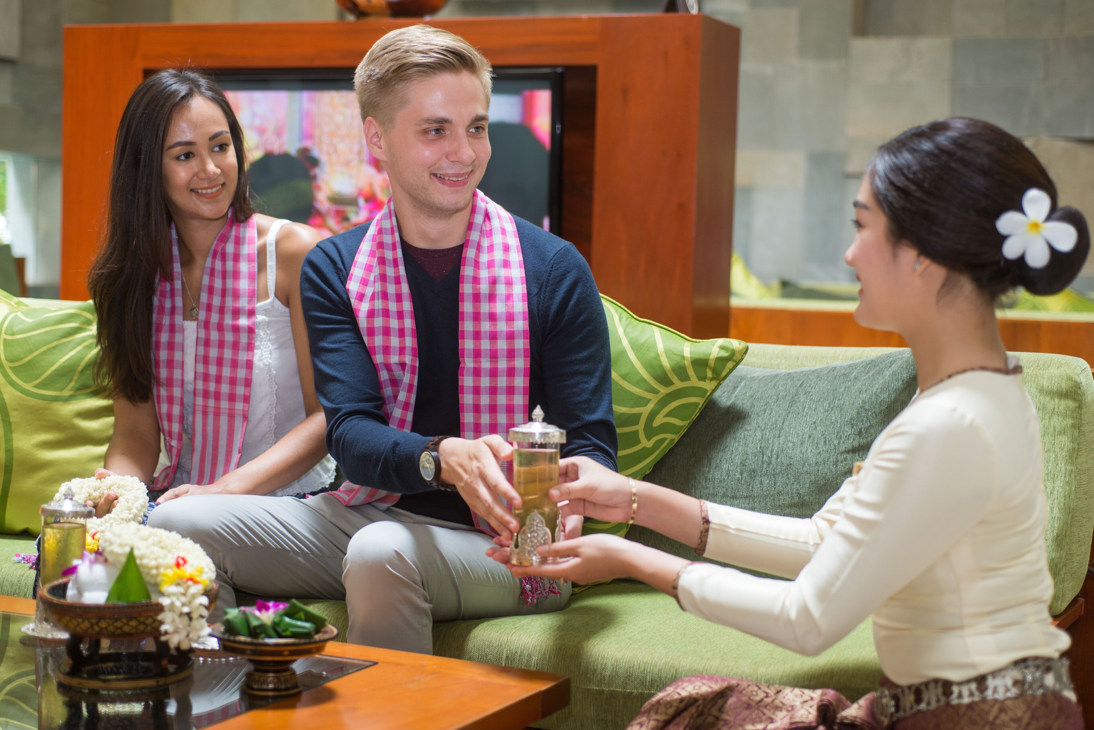 Eine Gruppe von Personen sitzt auf einem grünen Sofa und hält ein Getränk in der Hand, vor ihnen steht ein Couchtisch aus Holz.
