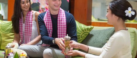 A group of people sitting on a green couch with a wooden coffee table in front of them, holding a glass of drink.