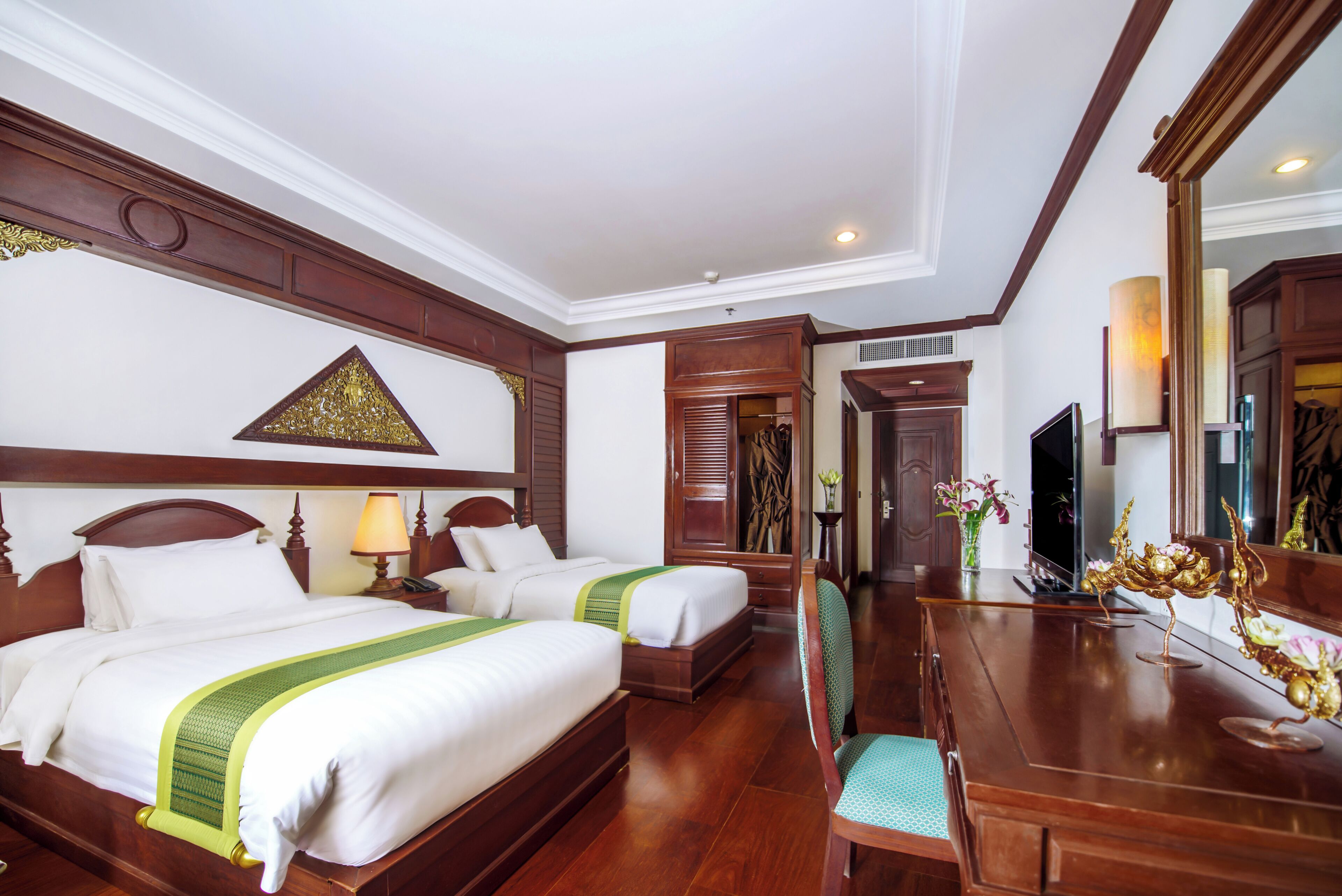 A hotel room with two beds, a wooden desk, a chair, a TV, and a mirror.