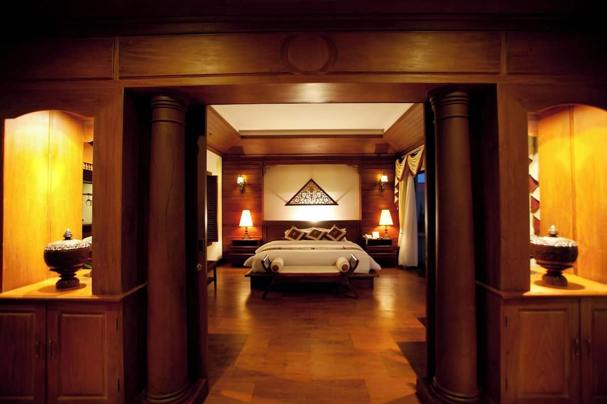 Une chambre d’hôtel avec un grand lit, des colonnes en bois et un lustre.