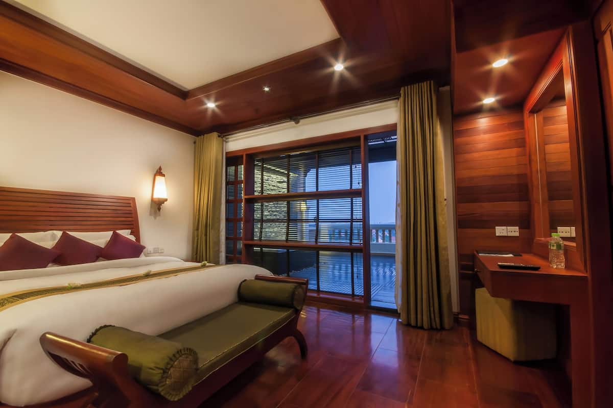 Une chambre d’hôtel avec un grand lit, un bureau en bois et une vue dégagée sur l’extérieur grâce à une grande fenêtre.