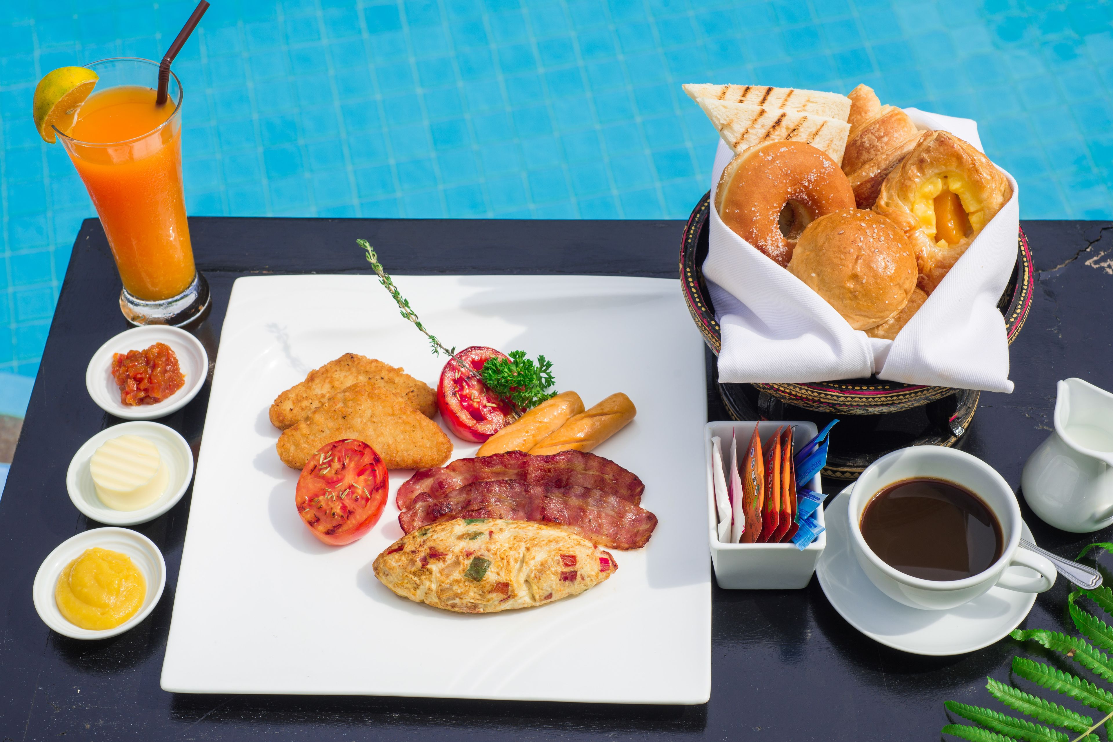 A breakfast tray with toast, eggs, bacon, and a glass of orange juice by a pool.