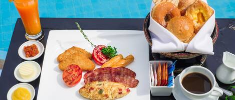 Bandeja de desayuno con tostadas, huevos, tocino y un vaso de jugo de naranja junto a una piscina.