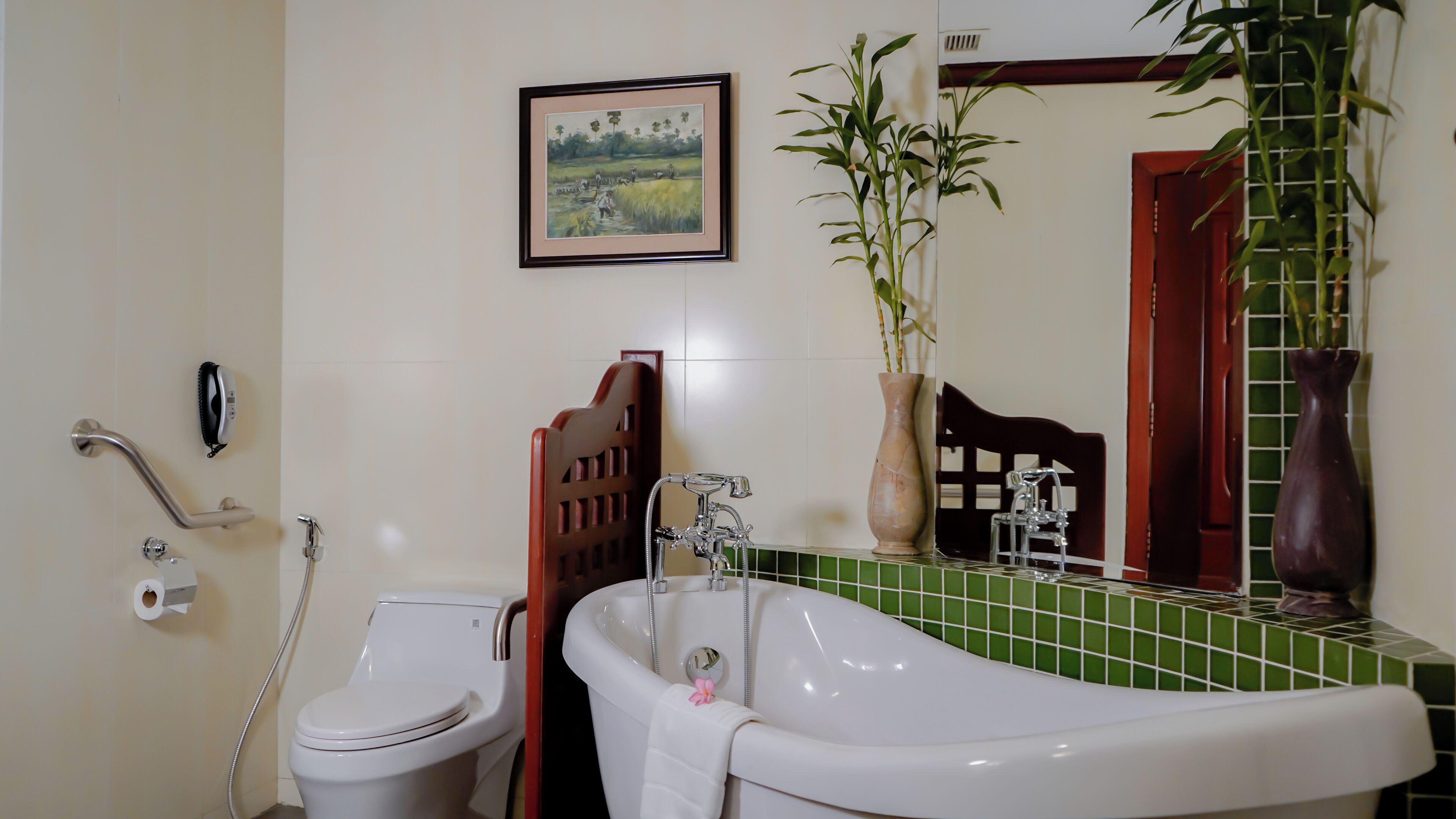 Une salle de bain avec une baignoire blanche, des toilettes, une douche, un tableau encadré au mur et une plante en pot.