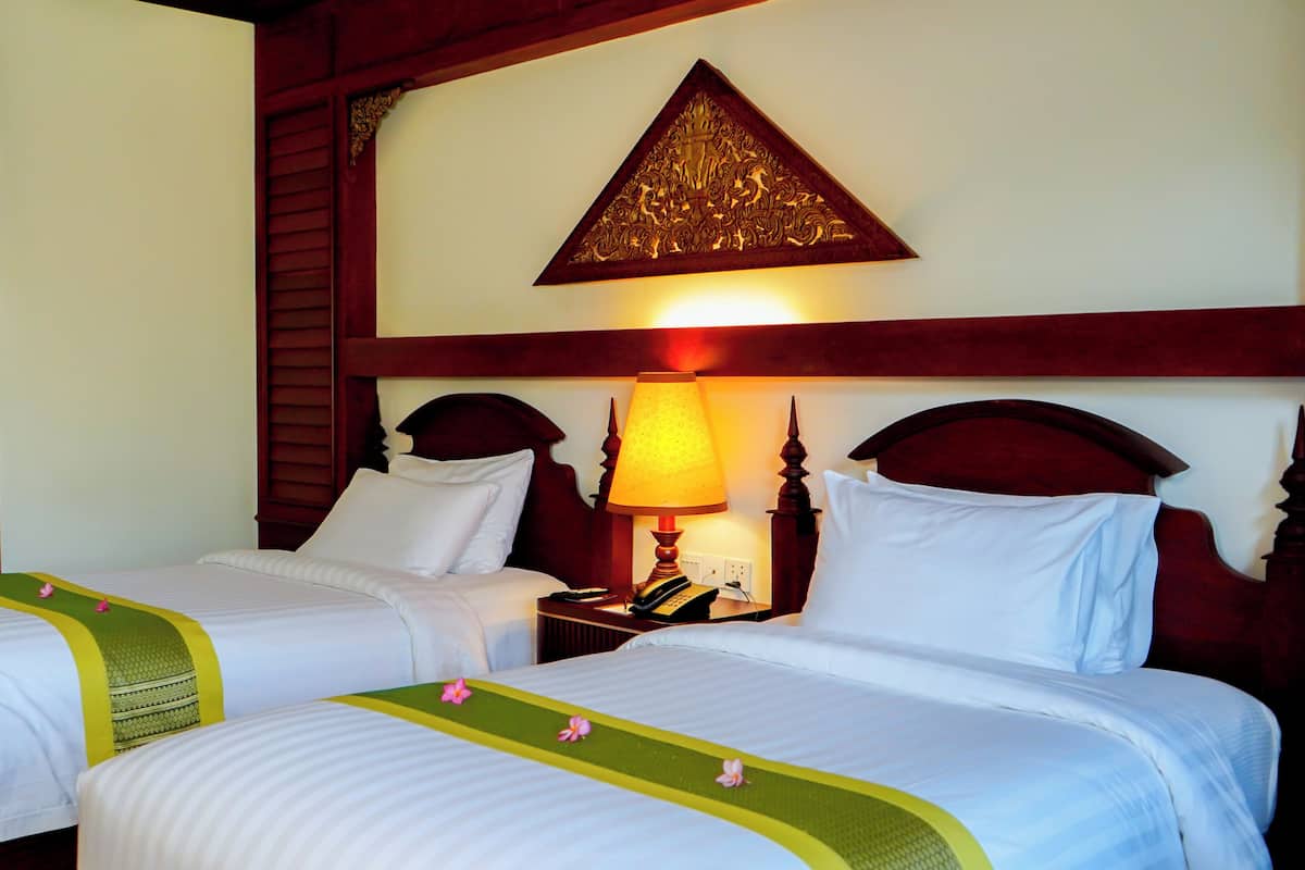 Une chambre d’hôtel avec deux lits, une tête de lit en bois, un élément décoratif mural et une lampe de chevet.