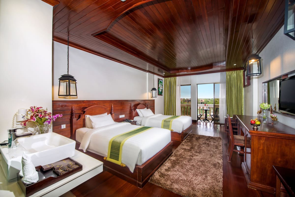 Une chambre d’hôtel avec deux lits, un plafond en bois, une grande fenêtre avec des rideaux, un lavabo et une télévision.