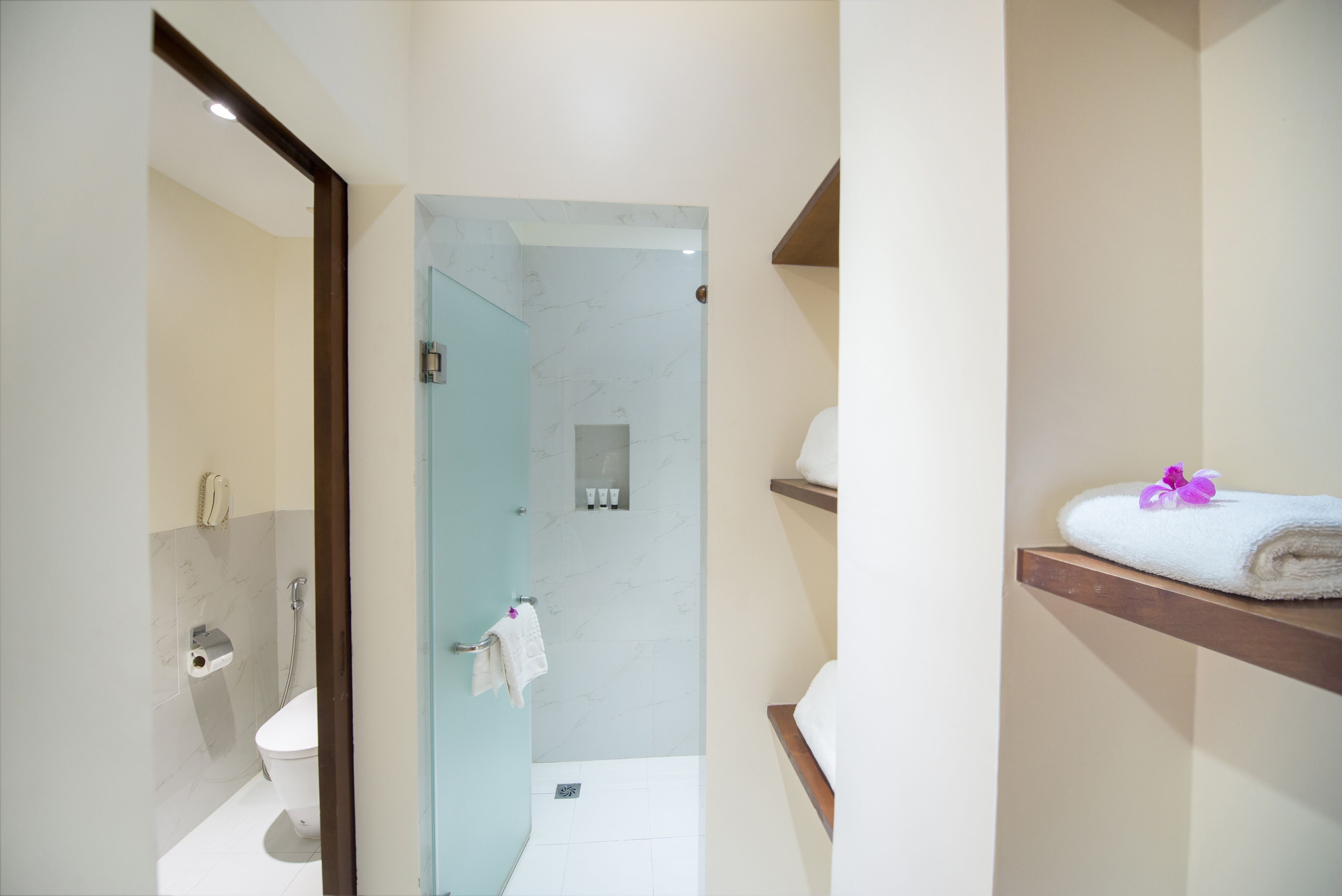 Ein modernes Badezimmer mit Duschabtrennung aus Glas, Toilette und Handtuchhalter mit Handtuch und einer violetten Blume.
