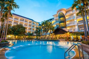A hotel with a large swimming pool, multiple balconies, and palm trees.