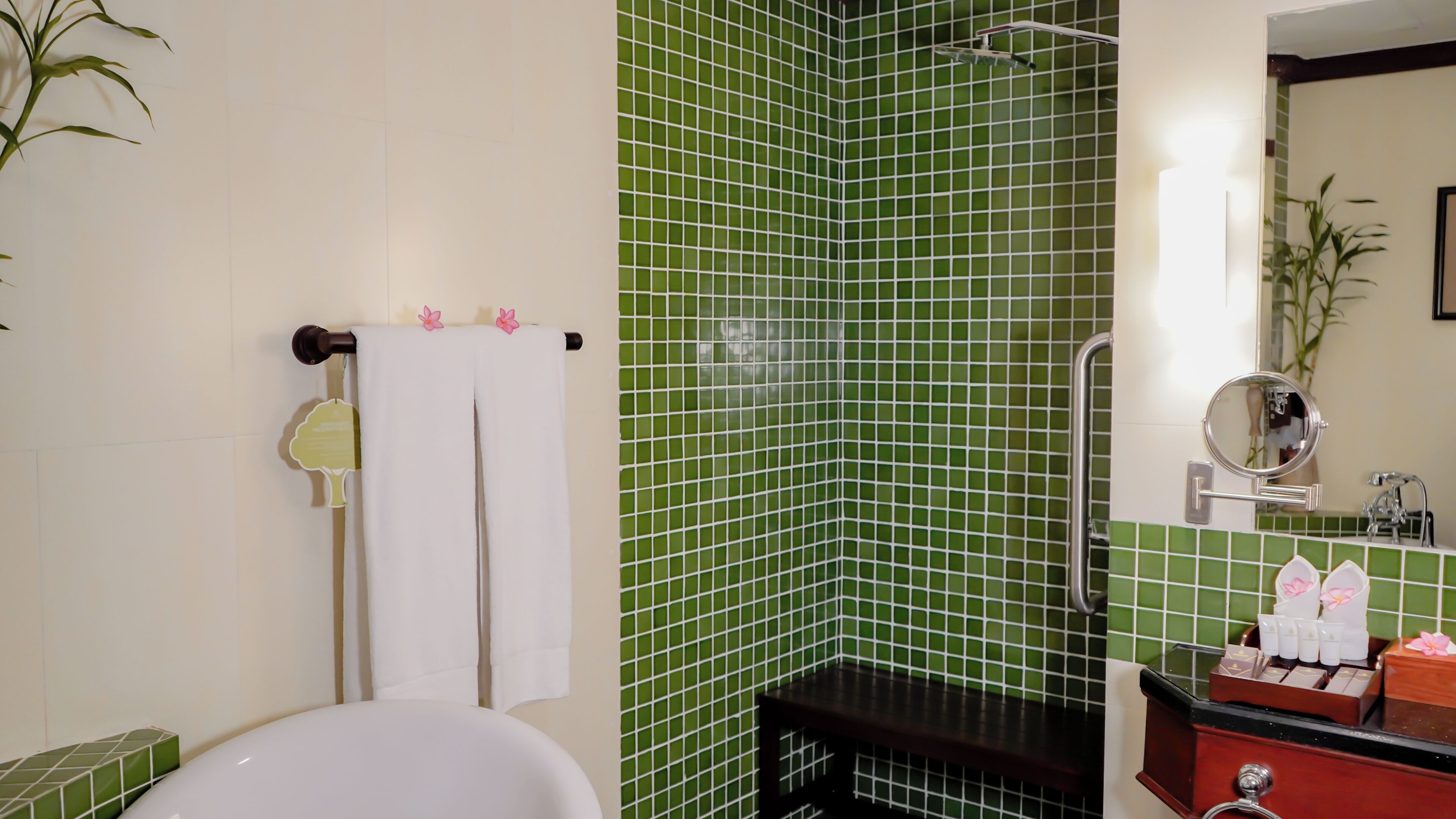 A bathroom with a green tiled shower wall, a white bathtub, and a vanity with toiletries.