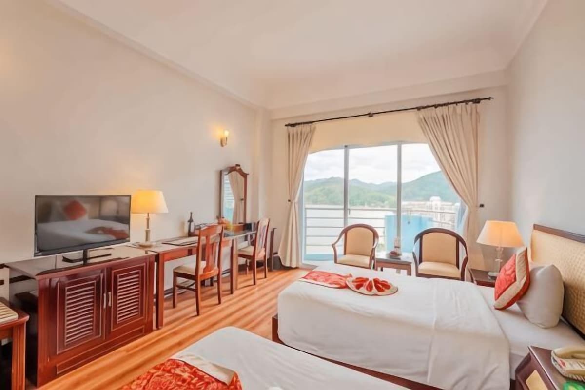 A hotel room with two beds, a desk with a TV, a chair, and a view of the outdoors.