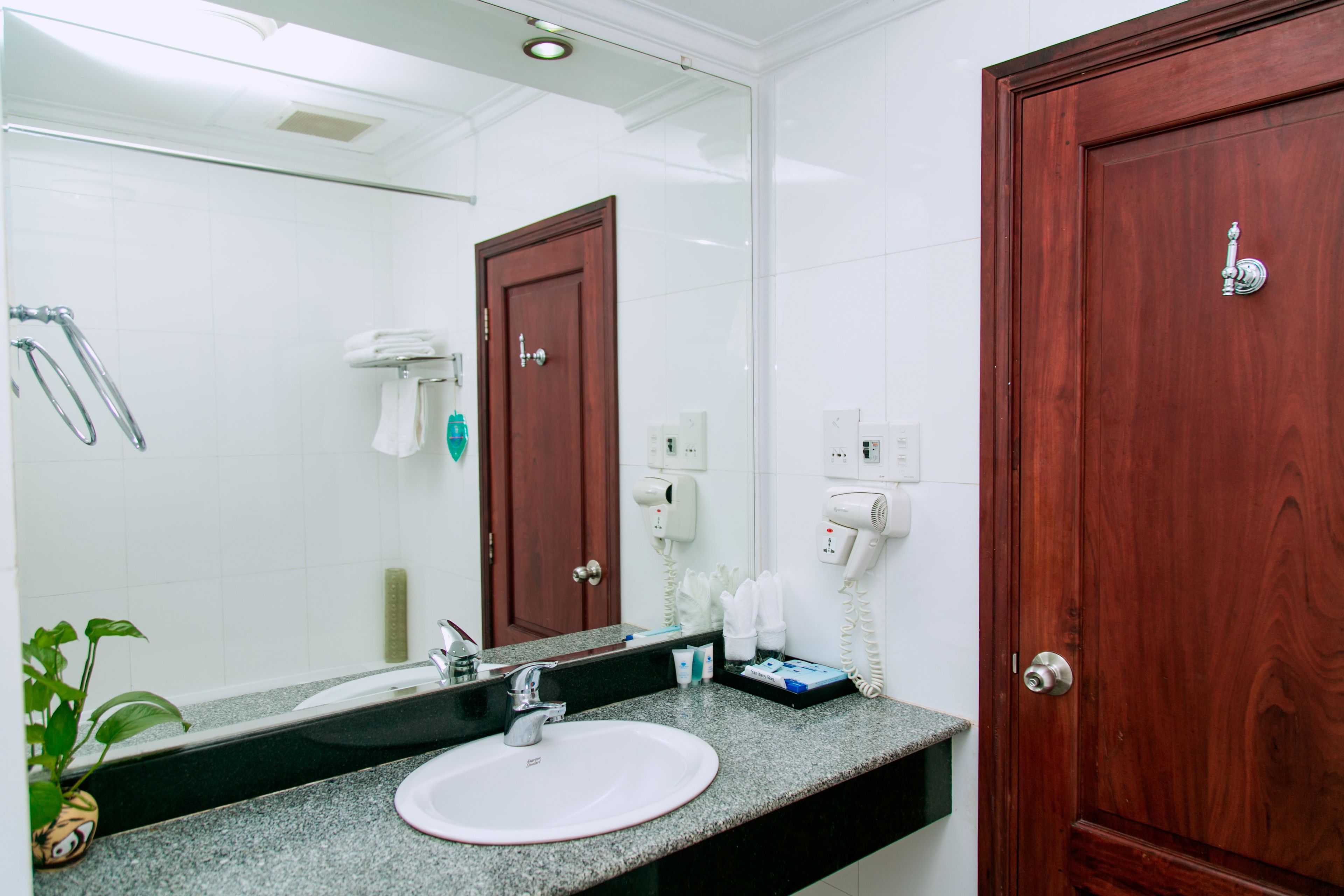 A bathroom with a white sink, a mirror, a towel rack, a hairdryer, and a wooden door.