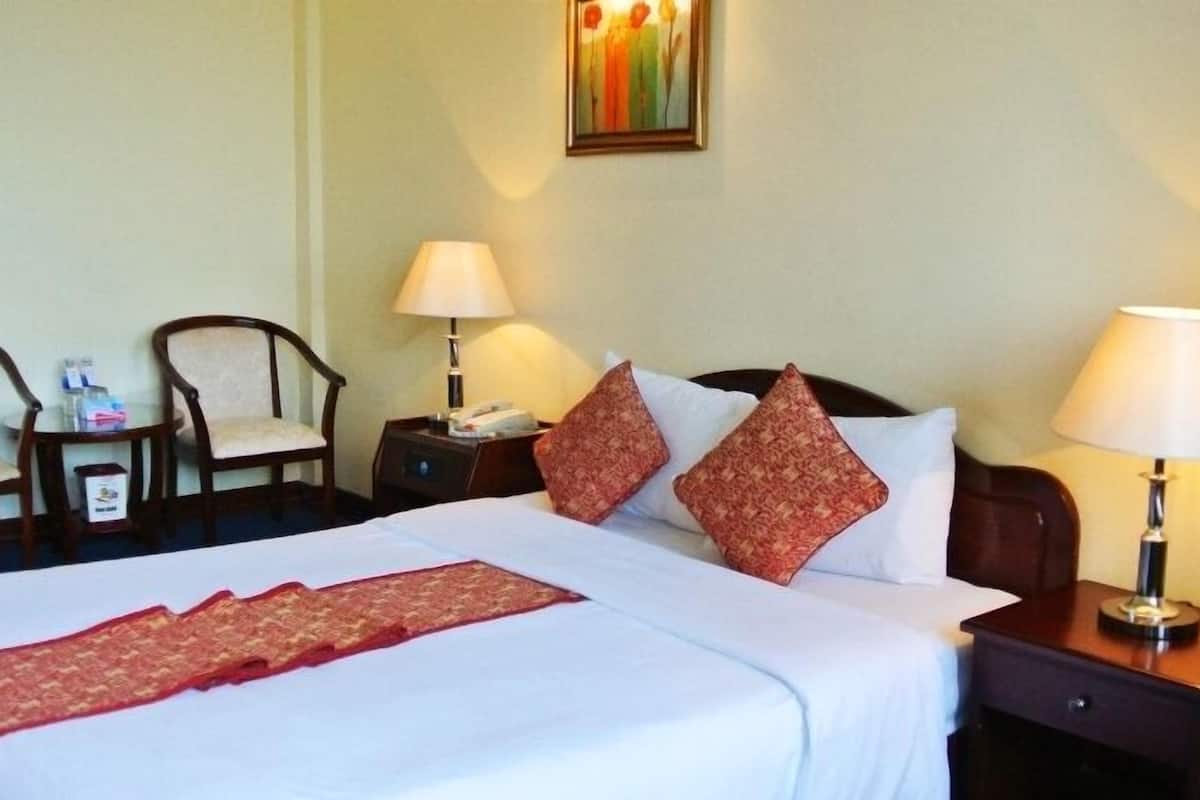 A hotel room with a large bed, two bedside tables, two lamps, a chair, and a small table with a phone and a box.