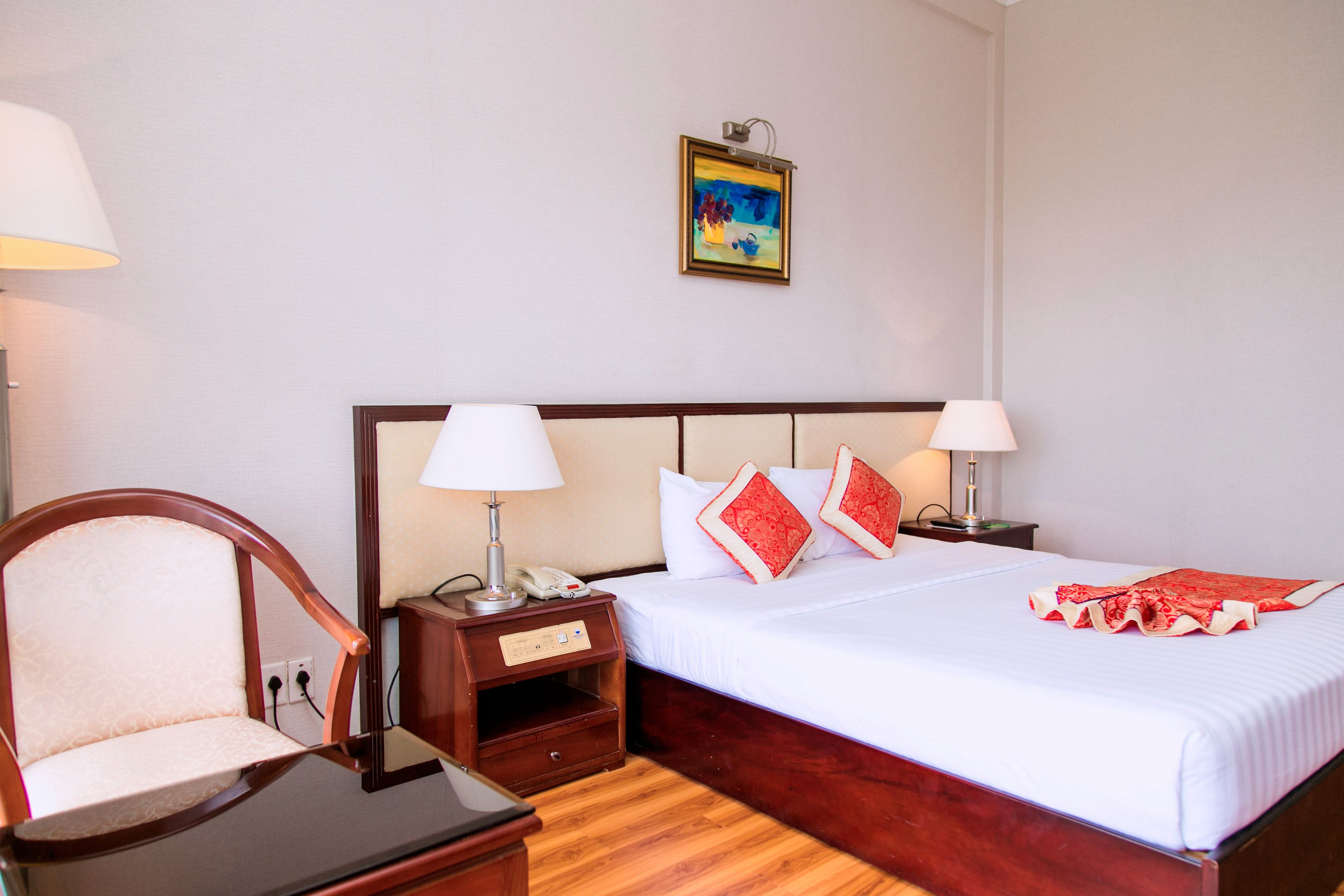 Una habitación de hotel con una cama de madera, dos mesitas de noche con lámparas, una silla y un cuadro en la pared.