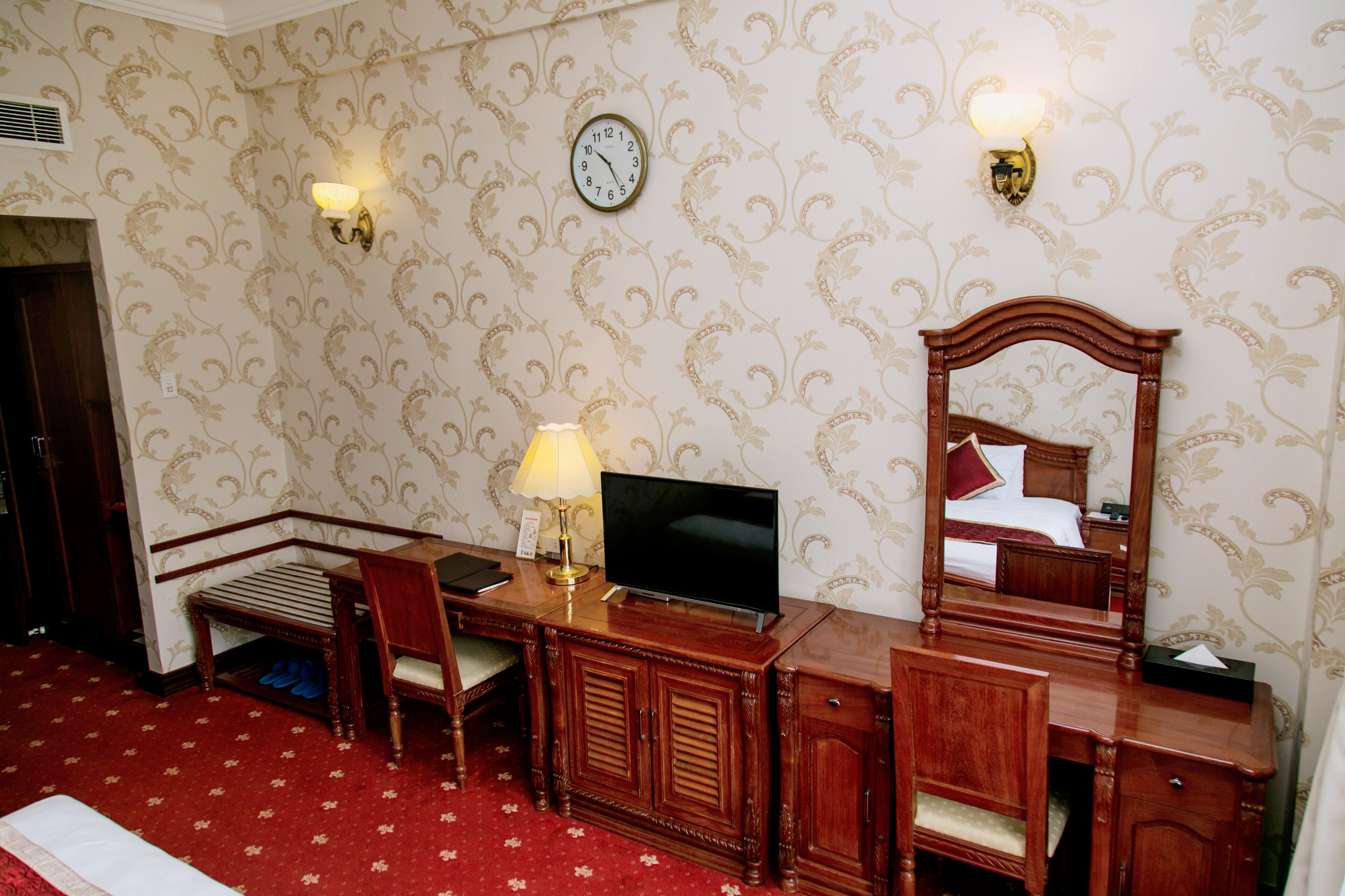 Een hotelkamer met een houten bureau, een televisie, een spiegel en een klok aan de muur.