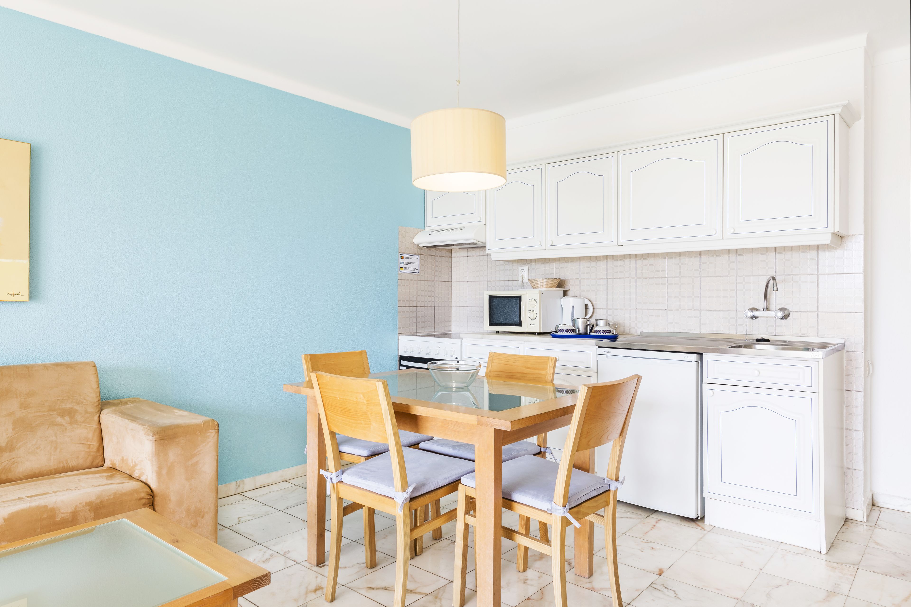A compact kitchen with white cabinets, a dining table with chairs, and a blue wall.
