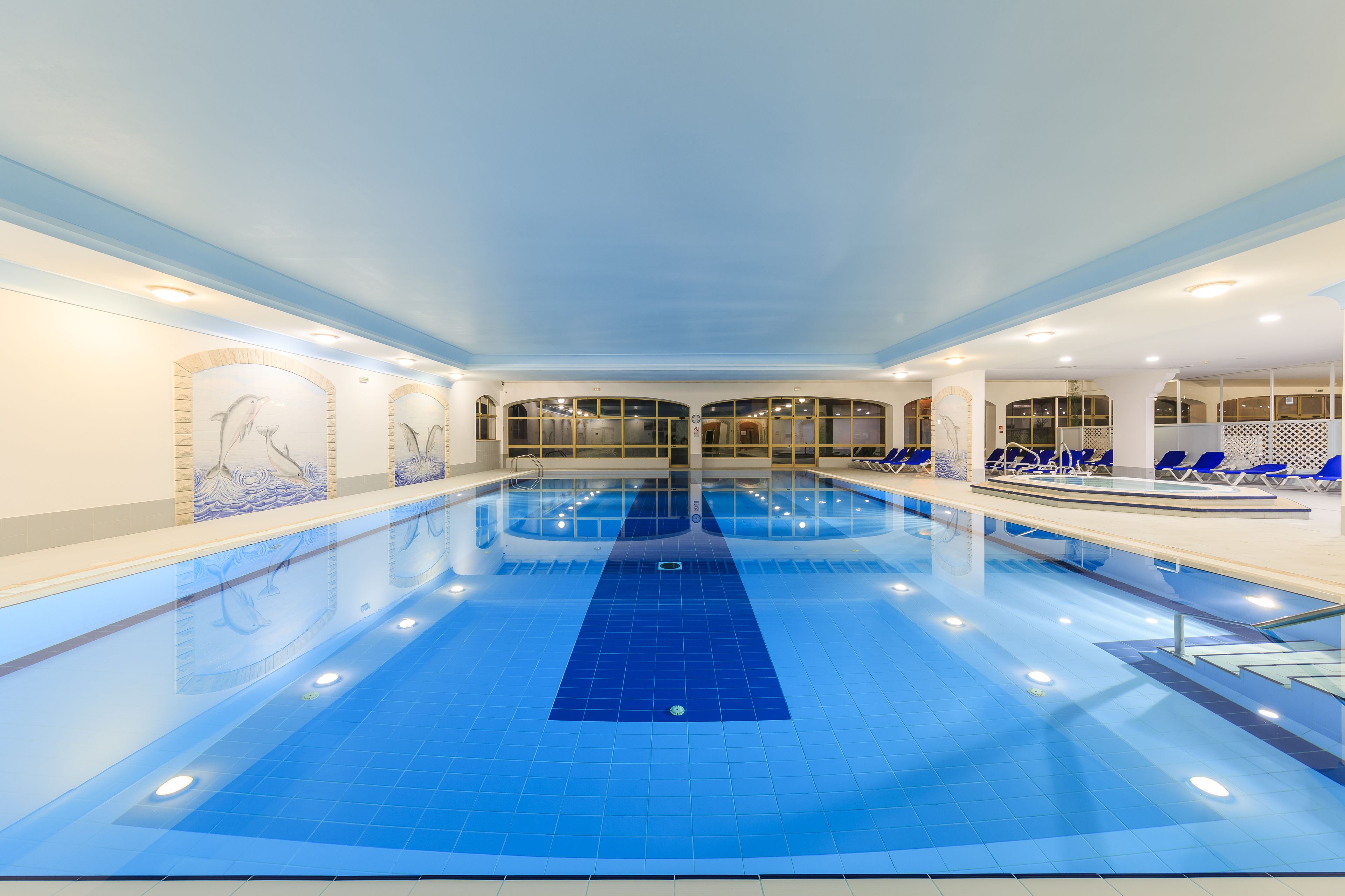 Una piscina interna con acqua cristallina, circondata da lettini e un pavimento piastrellato.