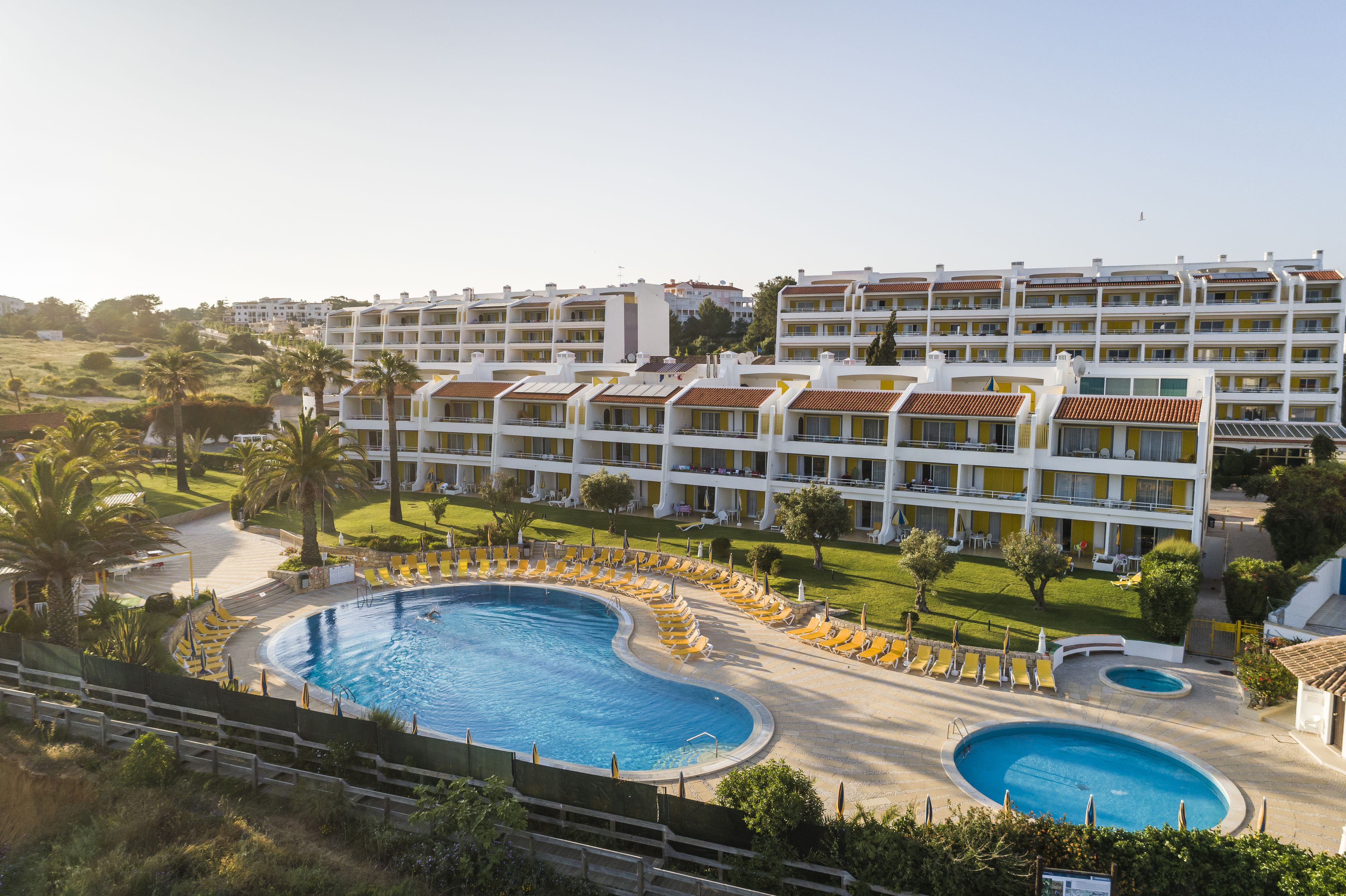 A hotel with multiple floors, a swimming pool, and a well-maintained lawn.