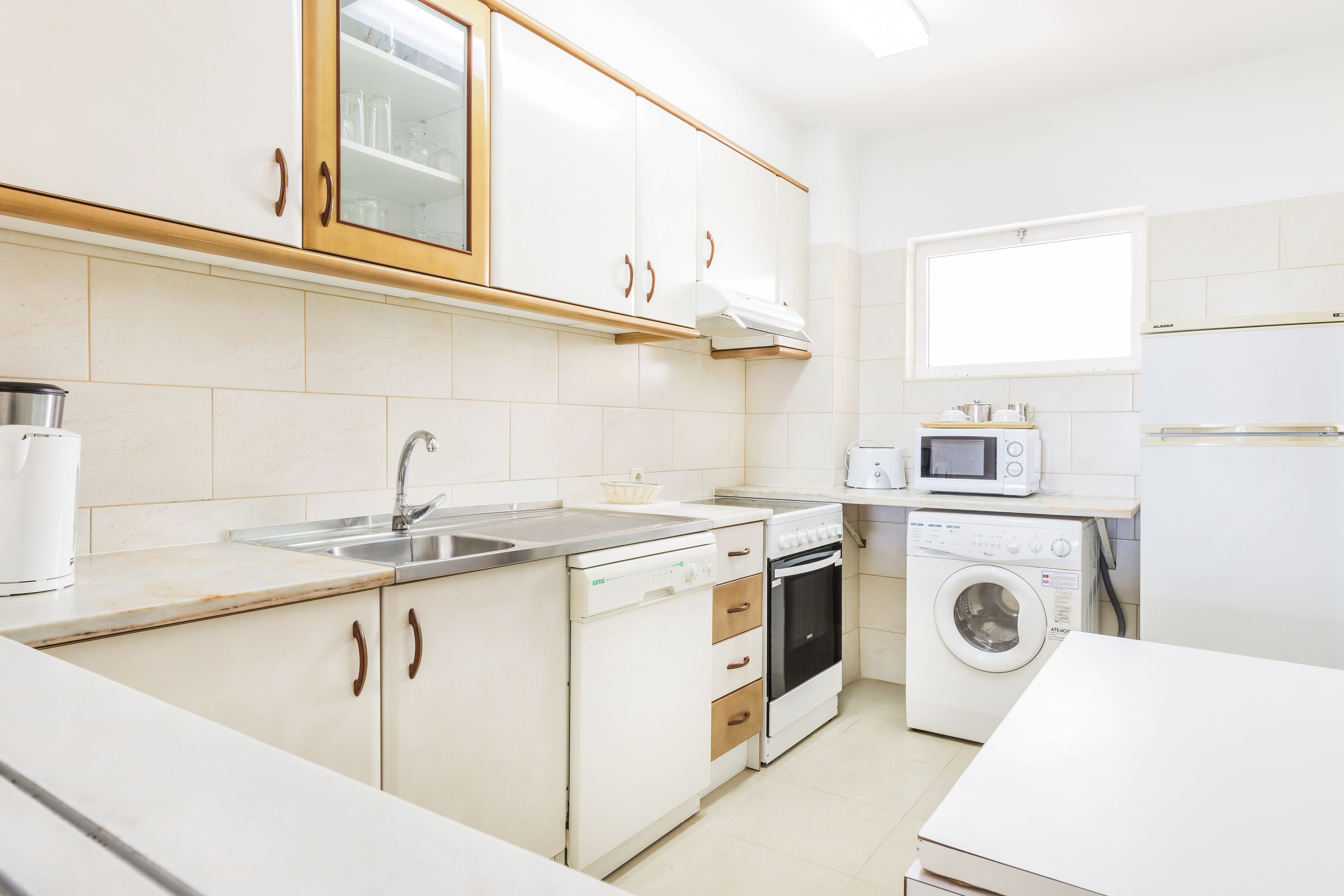 Una cocina moderna con armarios blancos, lavavajillas, horno, microondas y lavadora.