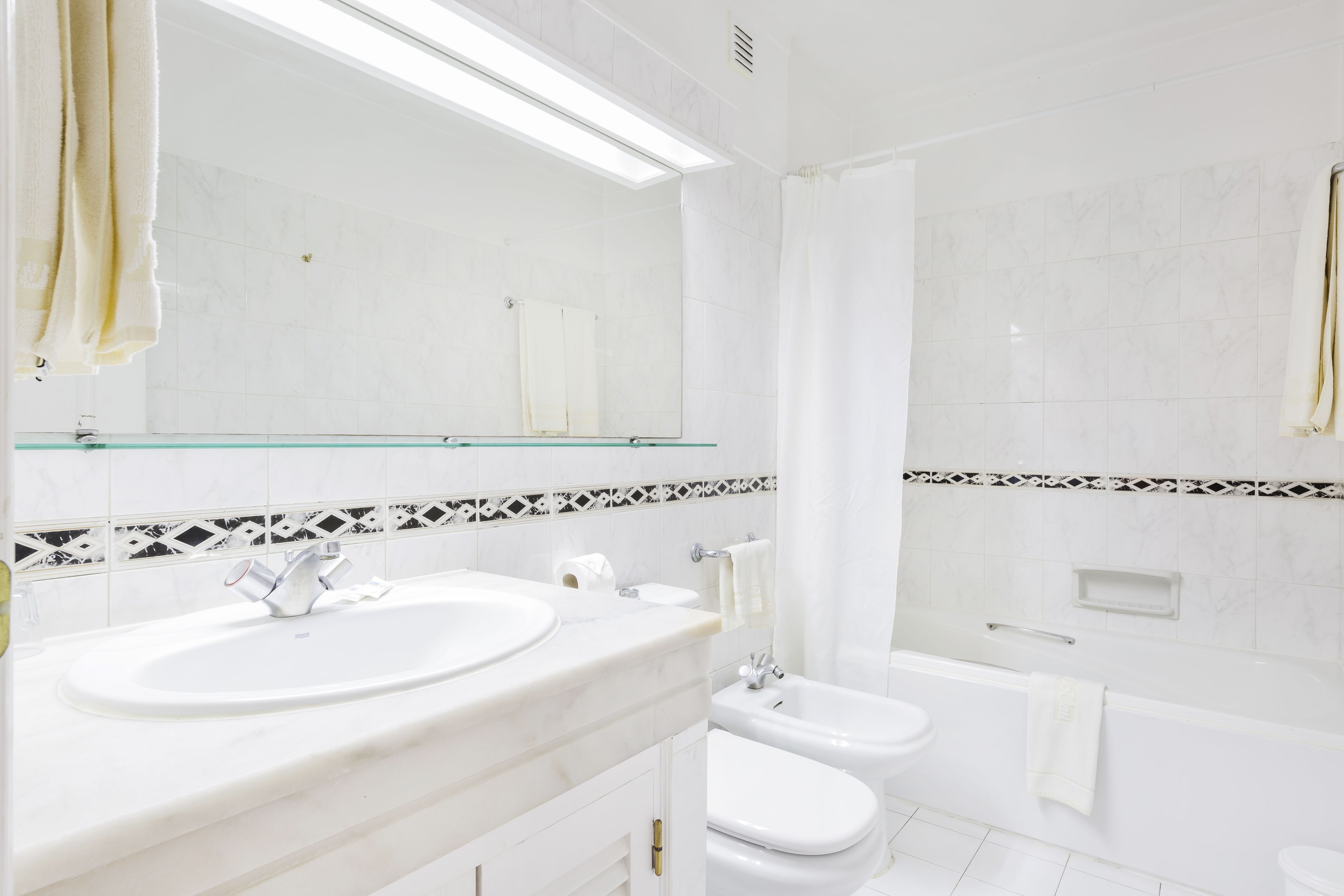 A modern bathroom with a large mirror, a sink, a bidet, a toilet, and a bathtub.