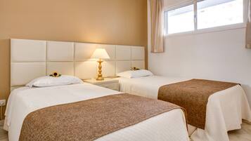 A hotel room with two beds, a nightstand with a lamp, and a window with curtains.