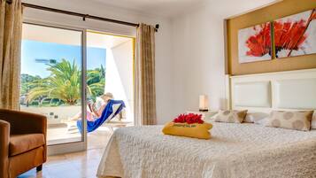 Une chambre d’hôtel avec un lit, une chaise, une vue sur un palmier et un tableau accroché au mur.