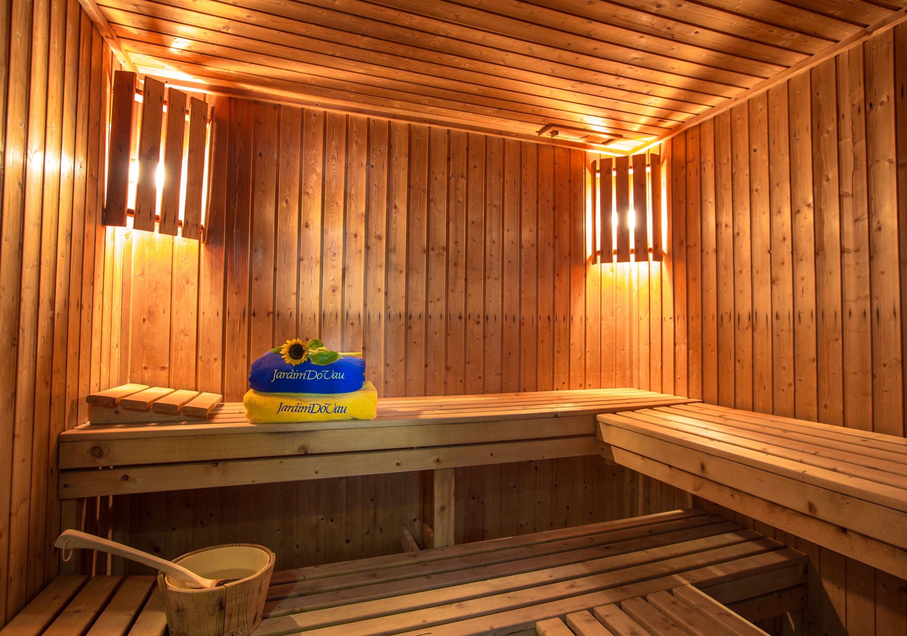 Una sauna con bancos de madera, un banco con un cubo, y una alfombra azul y amarilla sobre el banco.