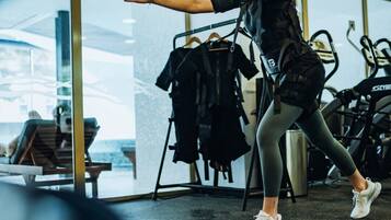 Una persona en un gimnasio con equipo de ejercicio y vista al mar a través de amplias ventanas.