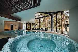 An indoor swimming pool with a tiled floor, a hot tub, and a seating area with black cushioned chairs.