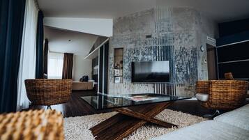 Relax in a stylish living space with a large flat-screen TV, glass coffee table, and two wicker armchairs.