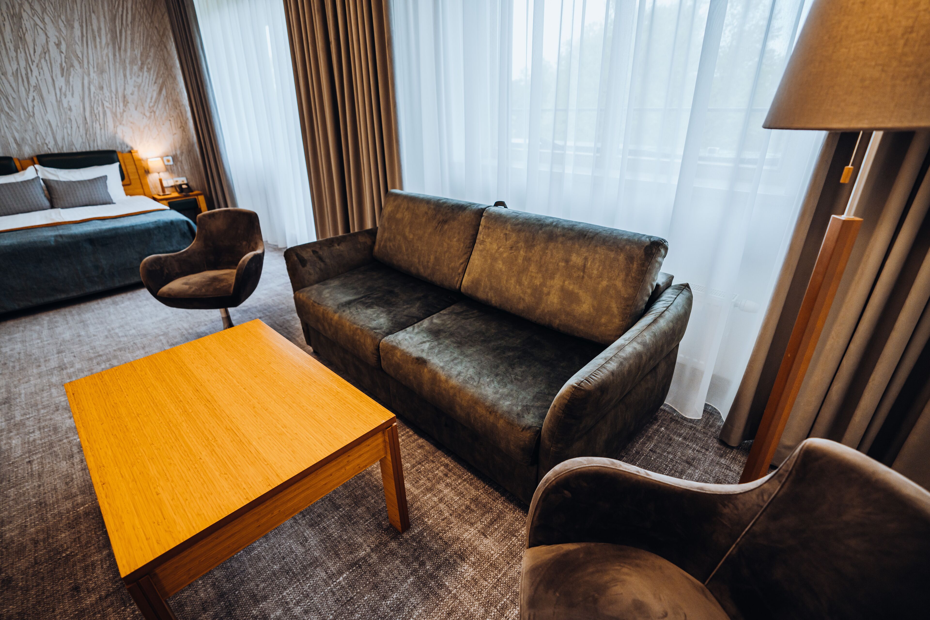Una habitación de hotel con un sofá, dos sillones, una mesa de centro de madera y una cama.