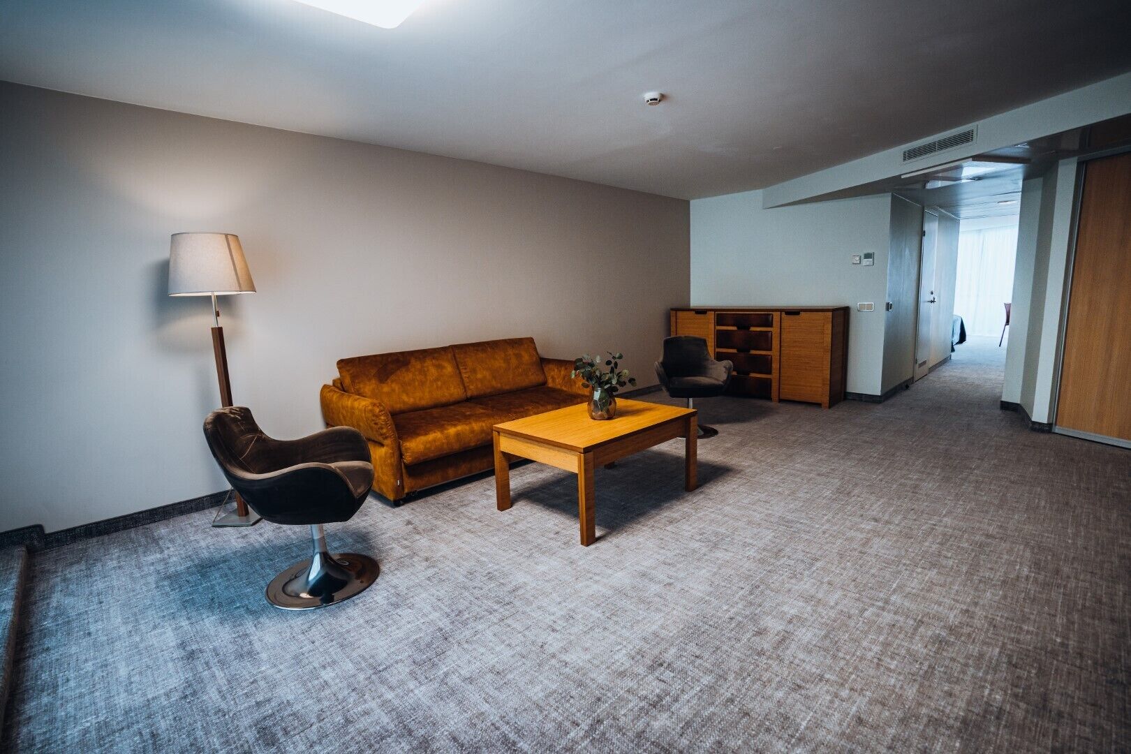 Sala de estar com sofá, poltrona, mesa de centro e abajur. Uma porta dá acesso a outro cômodo.