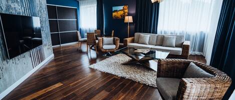 A modern living room with dark wooden flooring, a sofa, two armchairs, a coffee table, and a TV mounted on the wall.