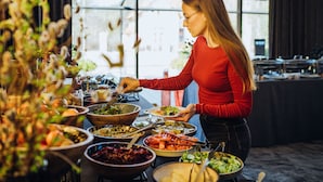 Een buffet met diverse gerechten en iemand die eten opschept.