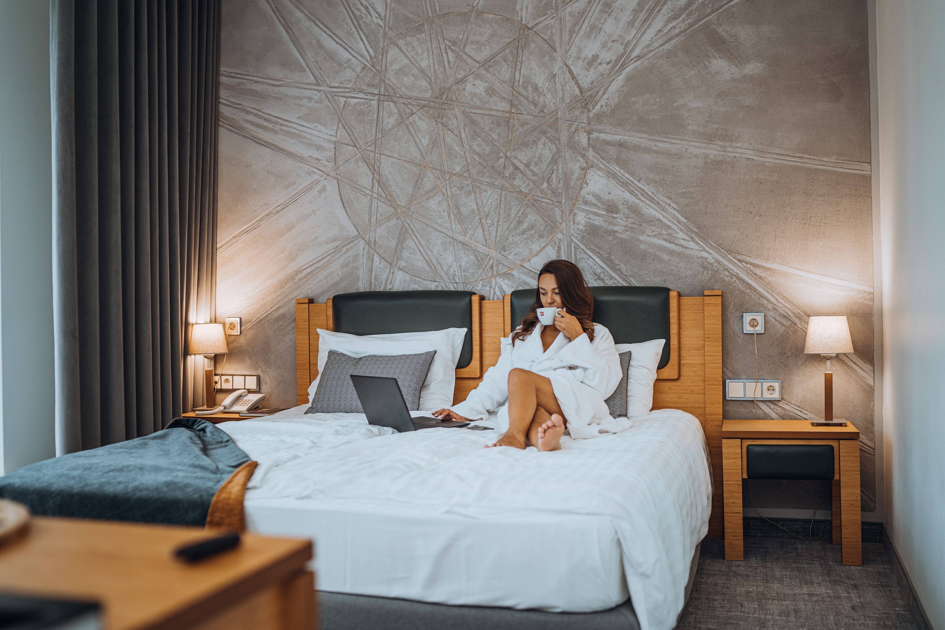 Una habitación de hotel con una cama, mesitas de noche, una lámpara, un teléfono y un ordenador portátil.