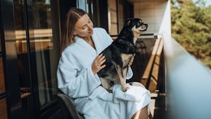Een persoon in een witte badjas zittend op een balkon met een hond.