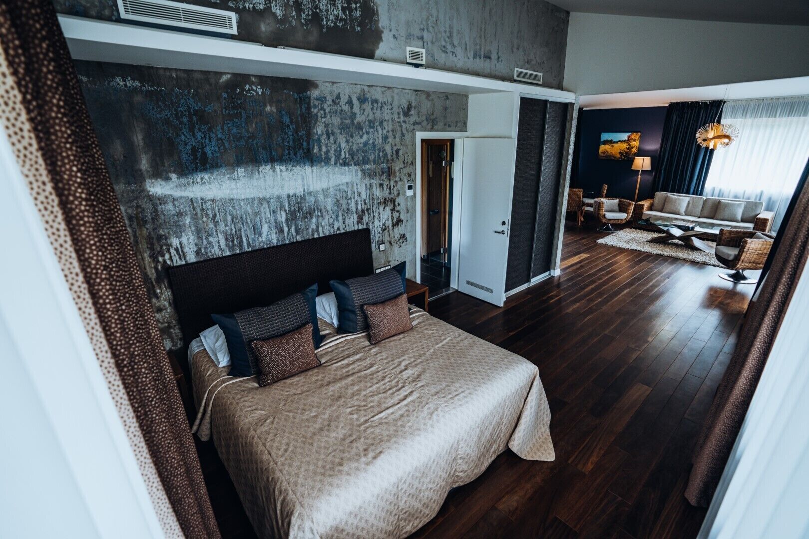 Une chambre à coucher moderne avec un grand lit, une tête de lit sombre et un mur d’accent en béton.