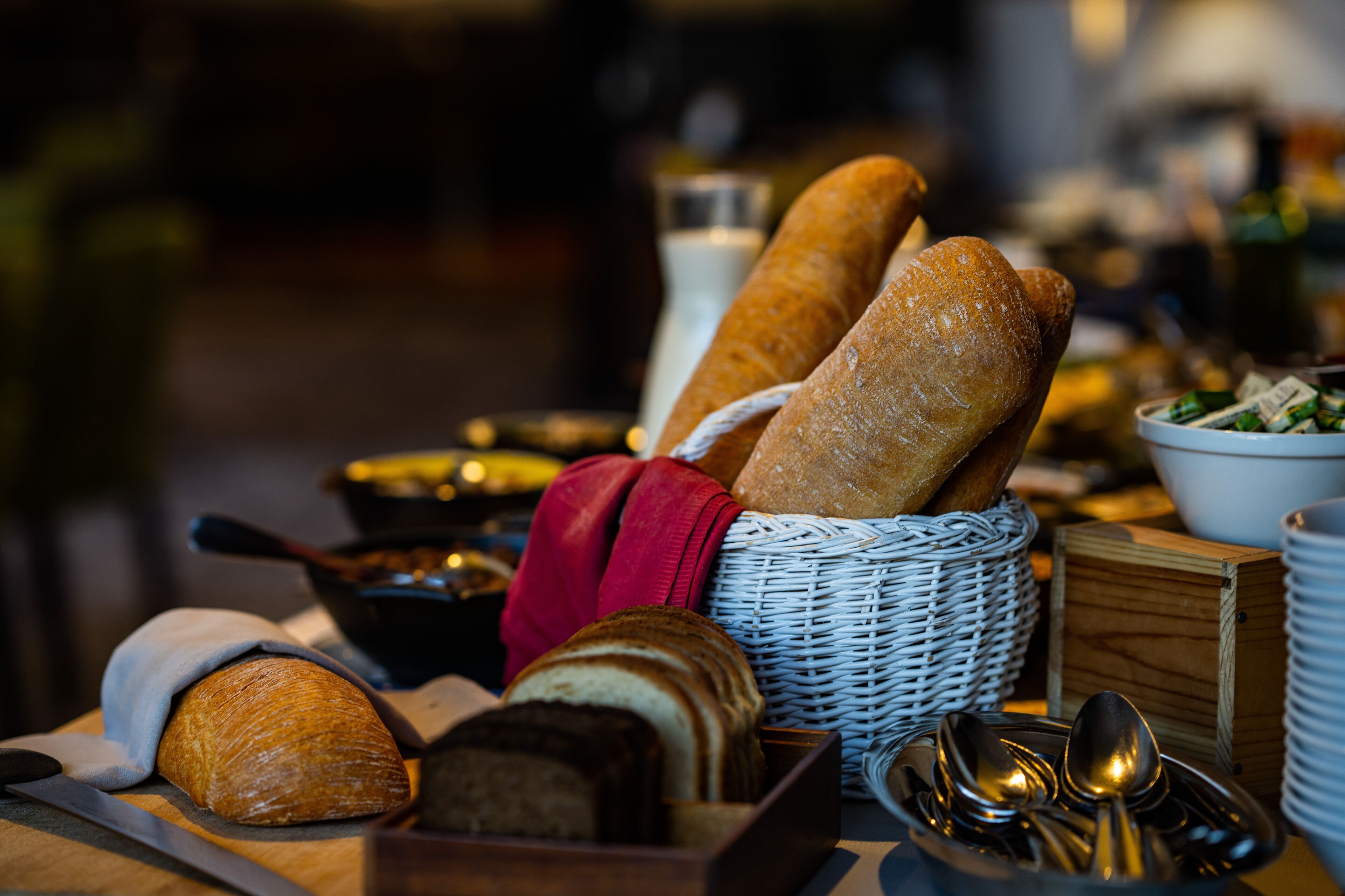 Uma mesa com pão, uma cesta e utensílios.