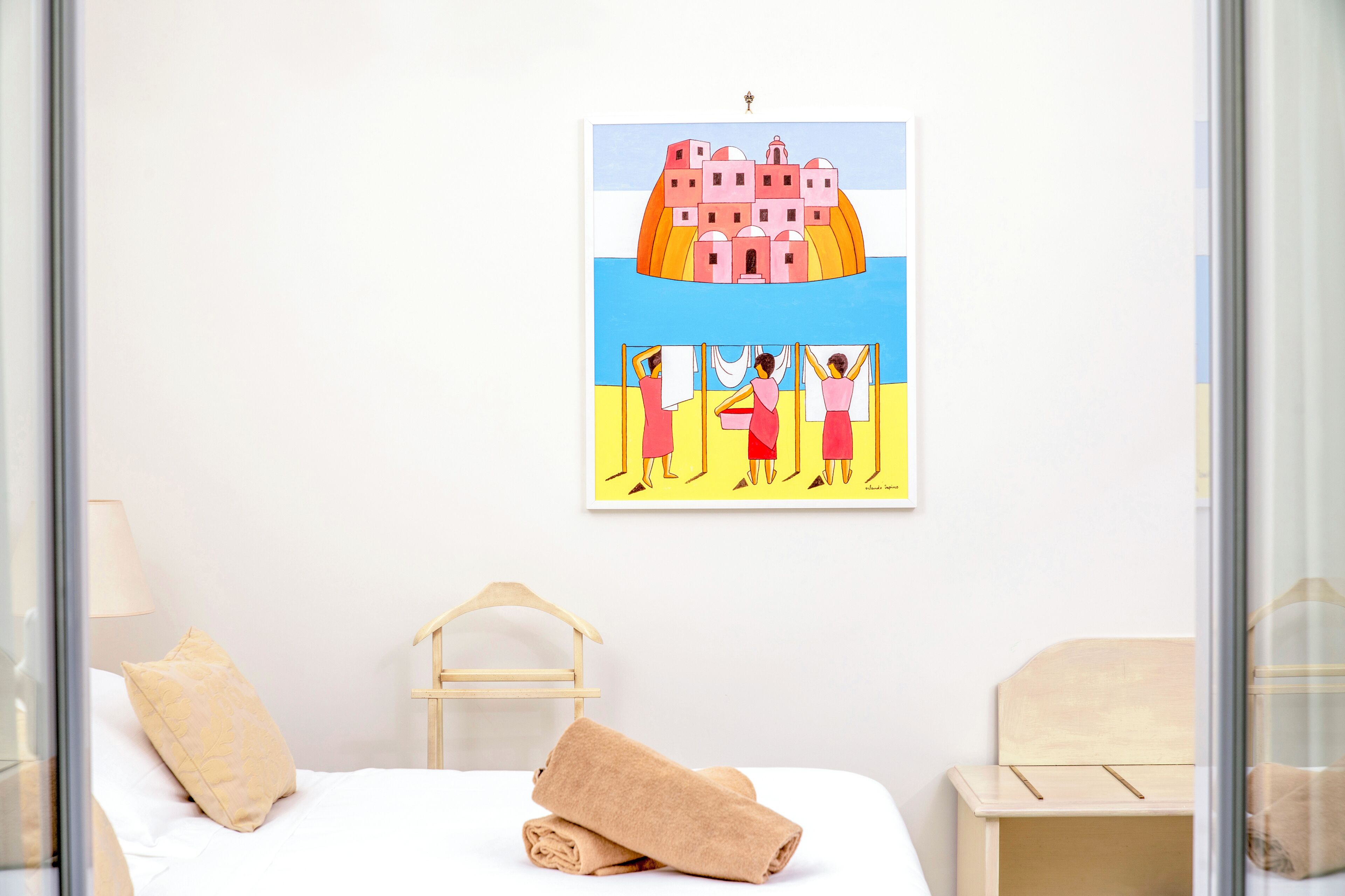 A hotel room with a bed, a wooden headboard, a rolled towel, and a framed artwork on the wall.
