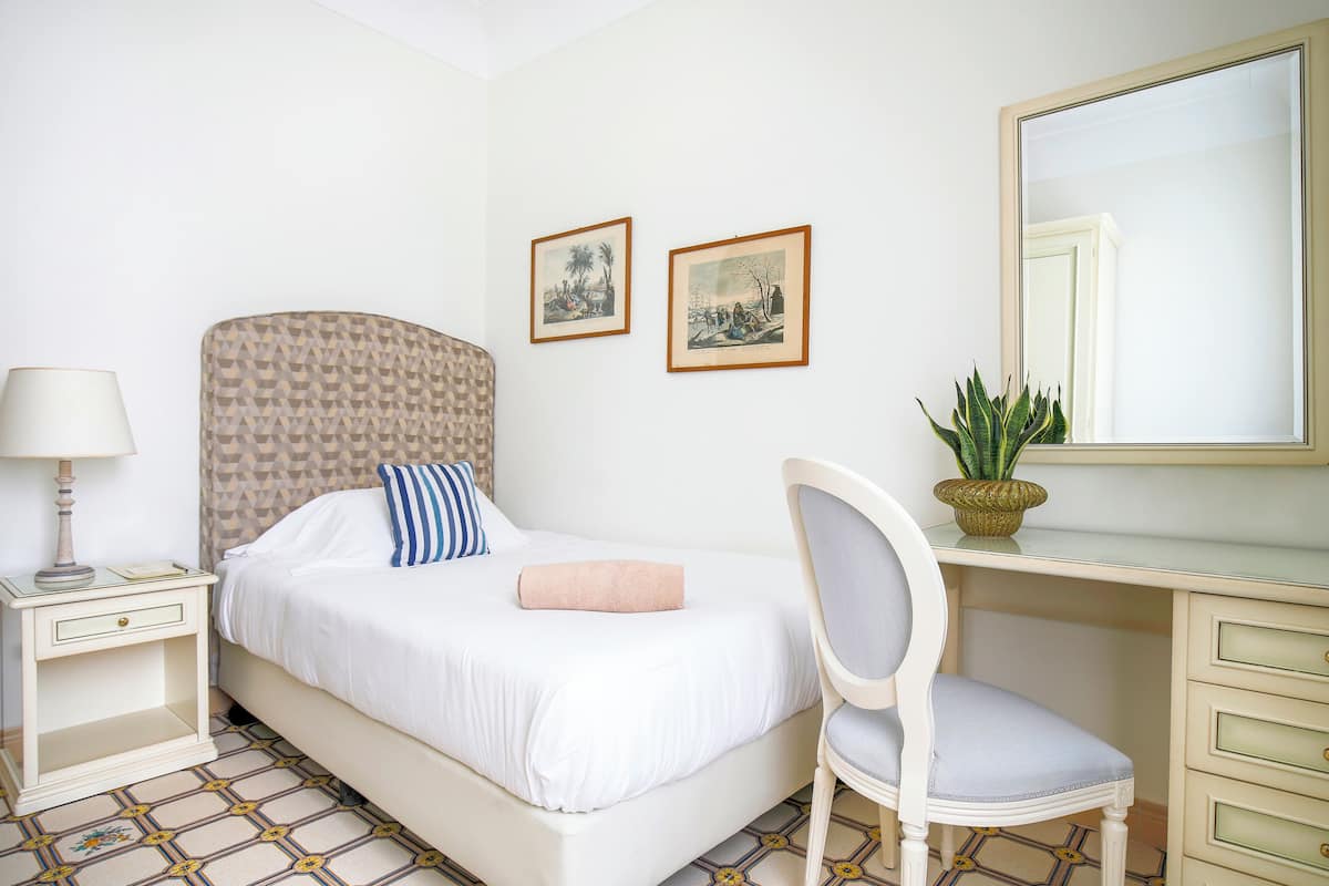 Une chambre d’hôtel avec un lit, un bureau, une chaise, une table de chevet, une lampe et deux tableaux encadrés au mur.